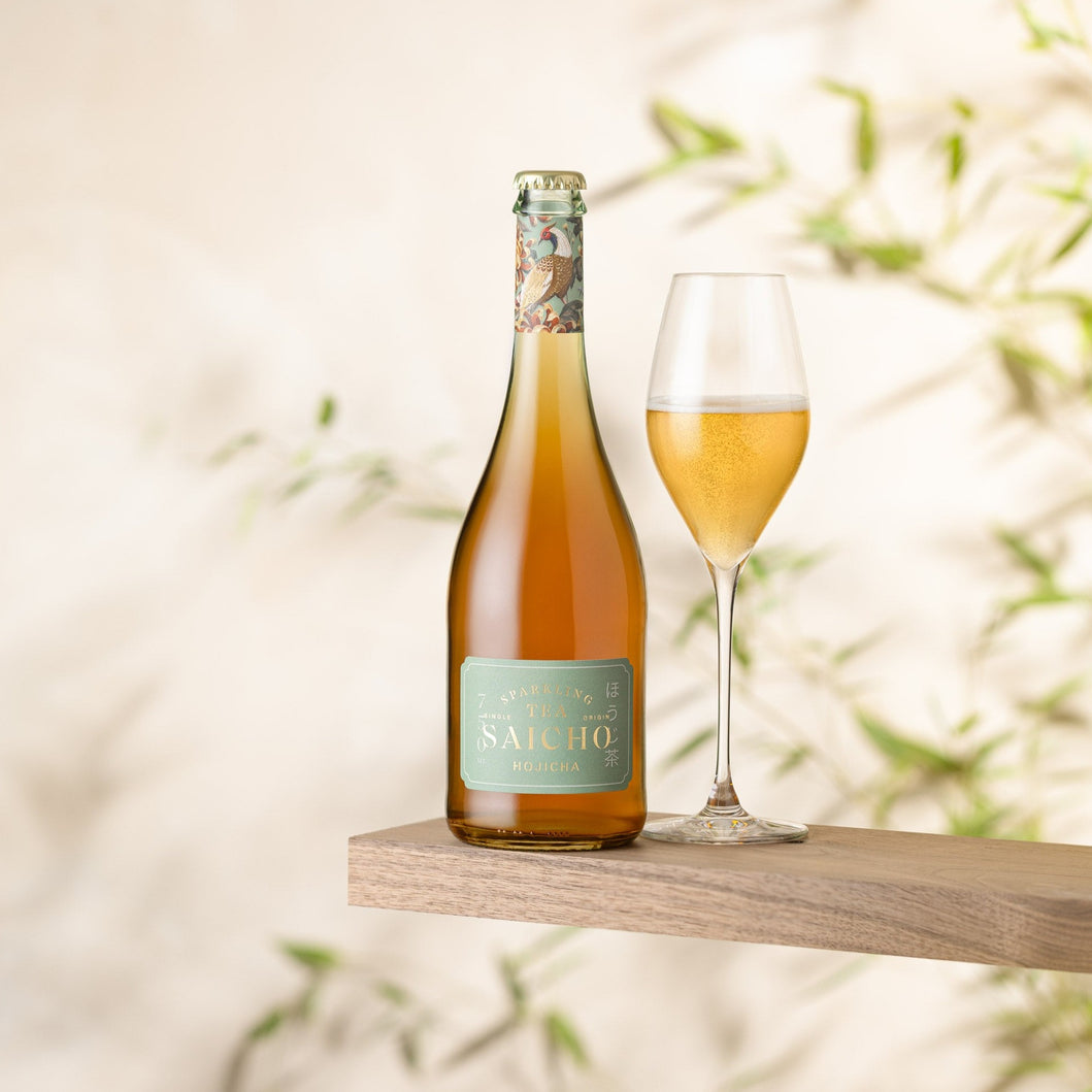 Bottle and glass of Saicho Hojicha Sparkling Tea on a wooden surface with a blurred natural background