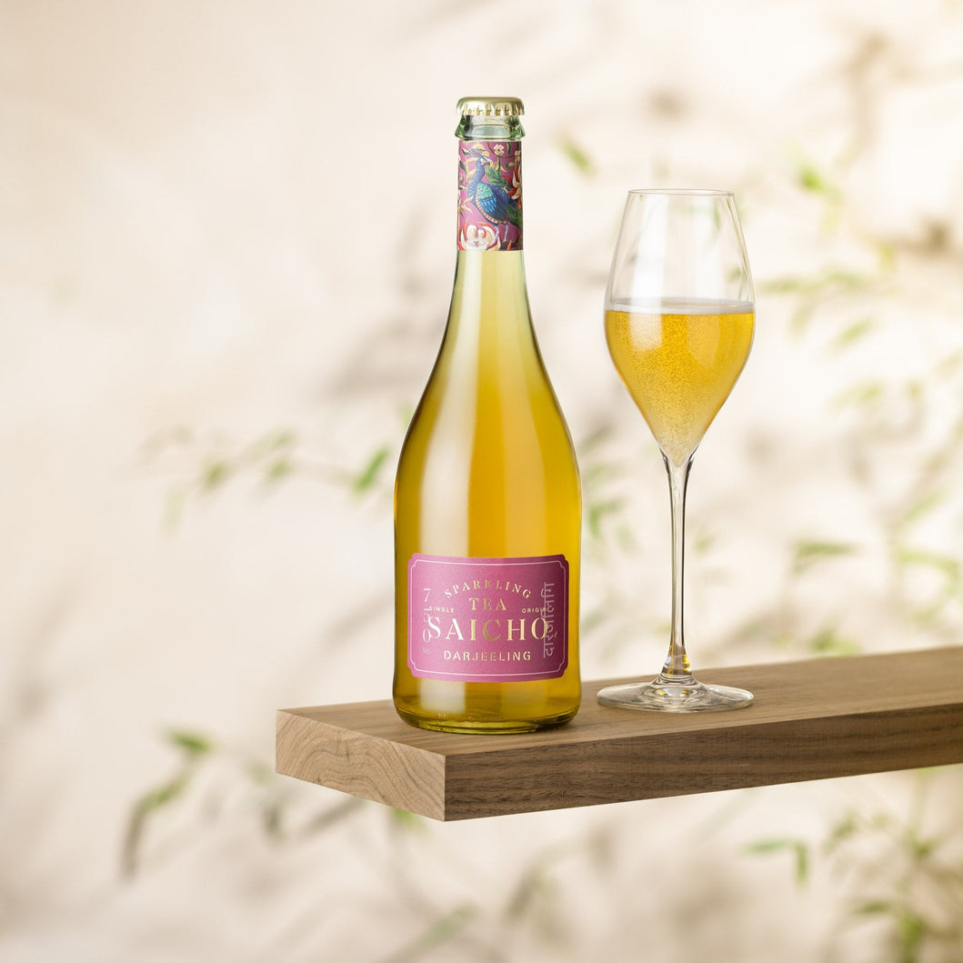 Bottle and glass of Saicho Darjeeling Sparking Tea on a wooden shelf with a blurred natural background