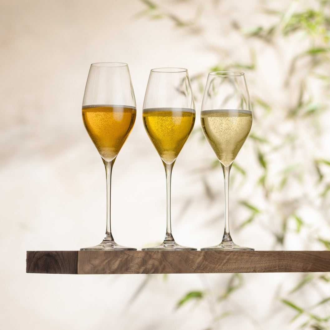 Three wine glasses with a light-colored liquid on a wooden shelf against a blurred natural background