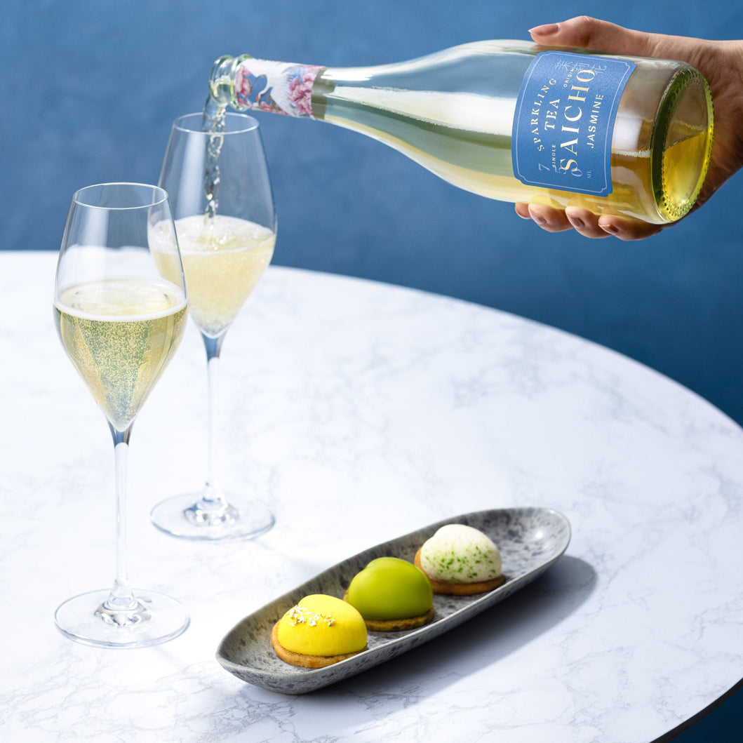 Bottle of Saicho Sparkling Jasmine Tea being poured into two glasses with pastries on a marble surface.