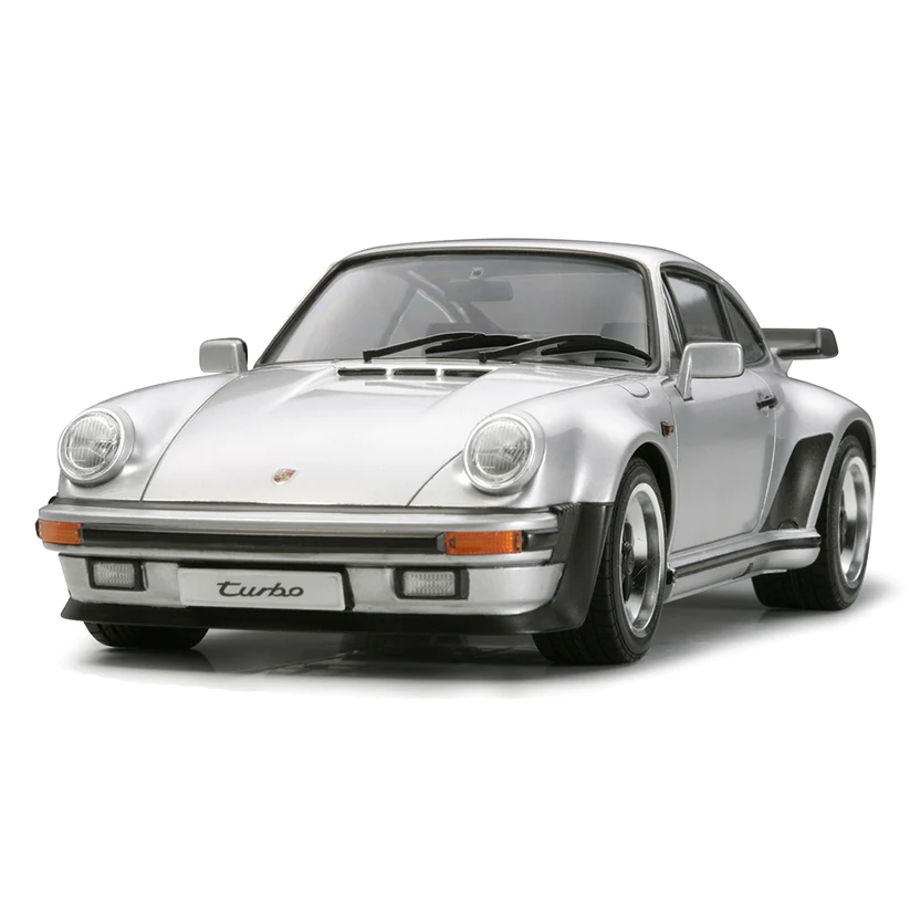 1/24 scale Tamiya Porsche 911 Turbo (1988) model kit featuring detailed recreations of the front and rear over-fenders, large rear wing, extra-wide tires, realistic engine underside with molded exhaust pipe, synthetic rubber tires with tread pattern, and metal transfers for mirrors and logo.